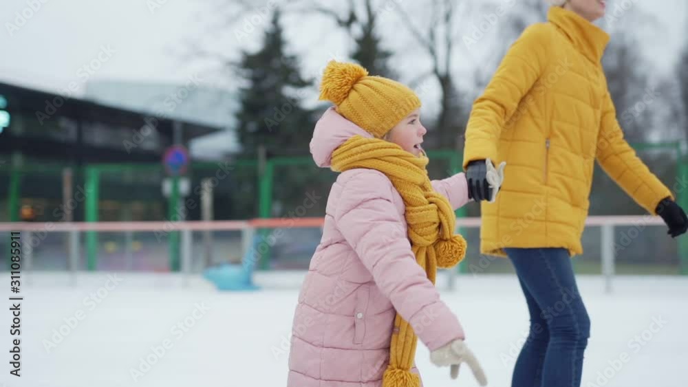 Tilt up tracking shot of mother and little daughter ice skating in slow motion holding hands into loving fathers embrace at outdoor ice rink Stock-Video | Adobe Stock