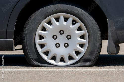 Flat tire on an unidentifiable black car. Low angle closeup view. No markings or identification on the car or tire.
