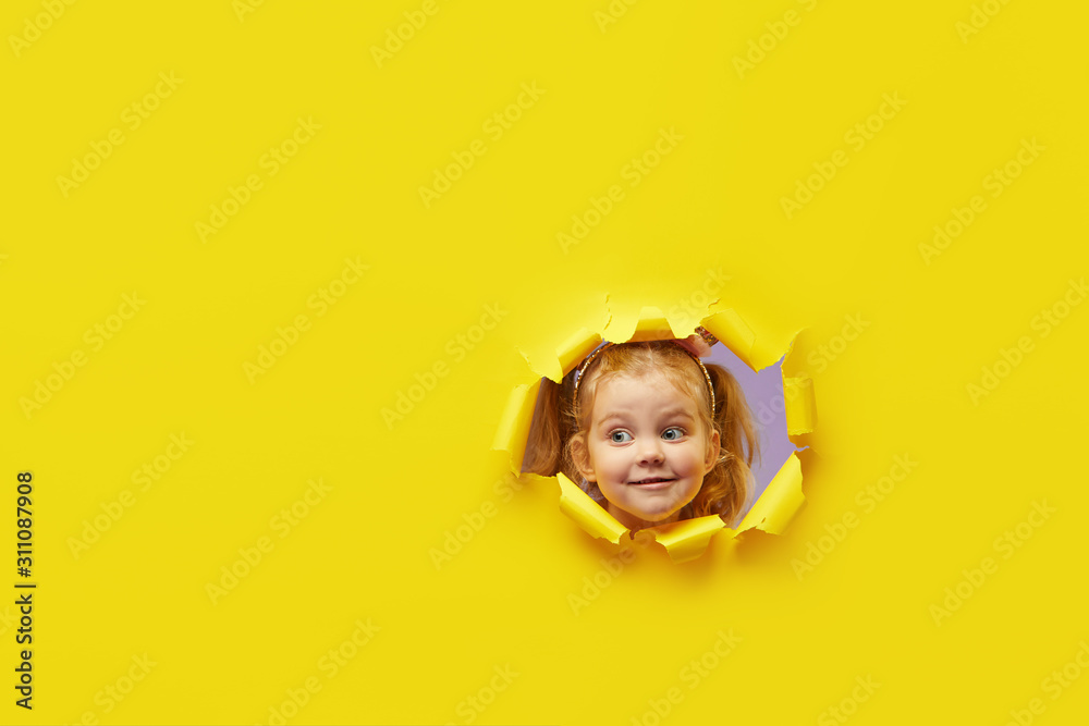 Little child looking, peeping through the bright yellow paper hole. Advertise children's goods. Wow and shocked funny face. Happy childhood concept. Copy space for text - obrazy, fototapety, plakaty 