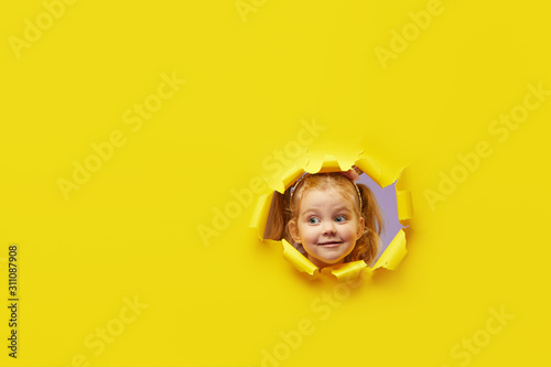 Little child looking, peeping through the bright yellow paper hole. Advertise children's goods. Wow and shocked funny face. Happy childhood concept. Copy space for text photo