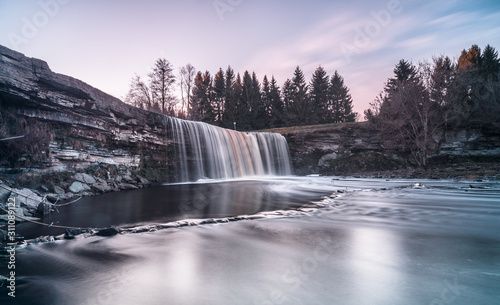 Fototapeta Naklejka Na Ścianę i Meble -  Long exposure photo of Jägala waterfall, 8 meters high and more than 50 meters wide fall in the lower course of the Jägala River. Estonia, Europe. Low sun casts various colors on the water.