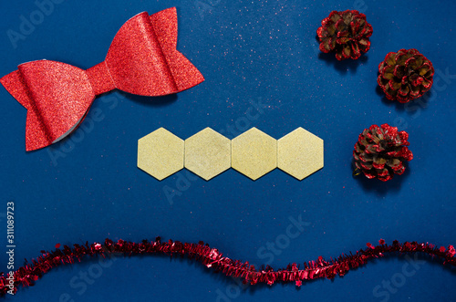 Gold wooden hexagons with copy space and red bow, cones and girland in a conceptual image of the coming new year. Over blue background.