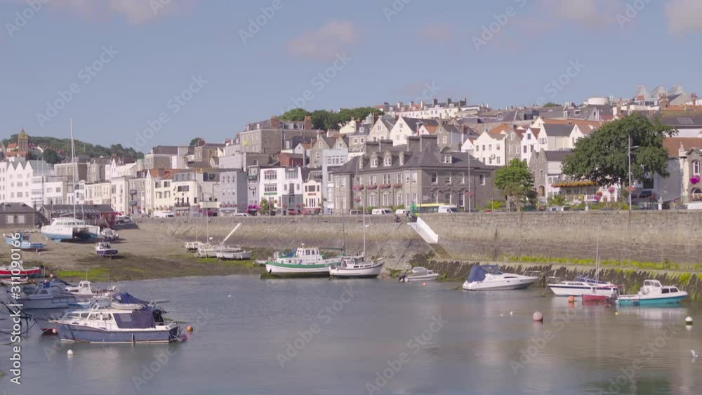 A handheld wide shot of a coastal seaside town with buildings and boats on a sunny day. Europe, UK A handheld wide shot of a coastal seaside town with buildings and boats on a sunny day. Europe, UK