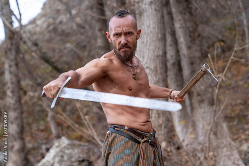 brutal viking with a naked torso and weapons in his hands photo