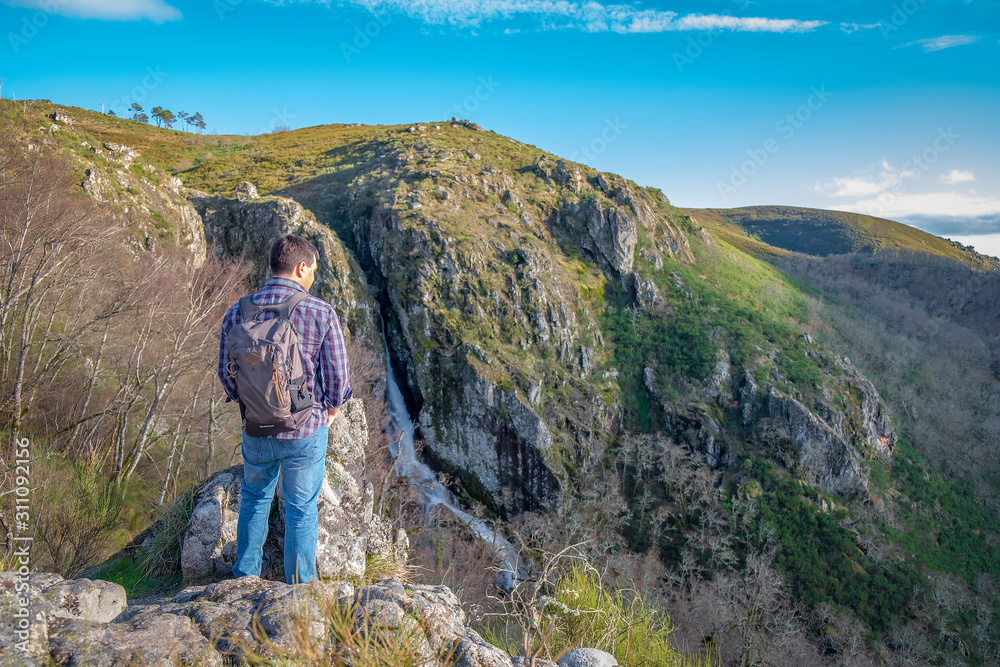 homem com mochila às costas a olhar para a paisagem cachoeira na montanha