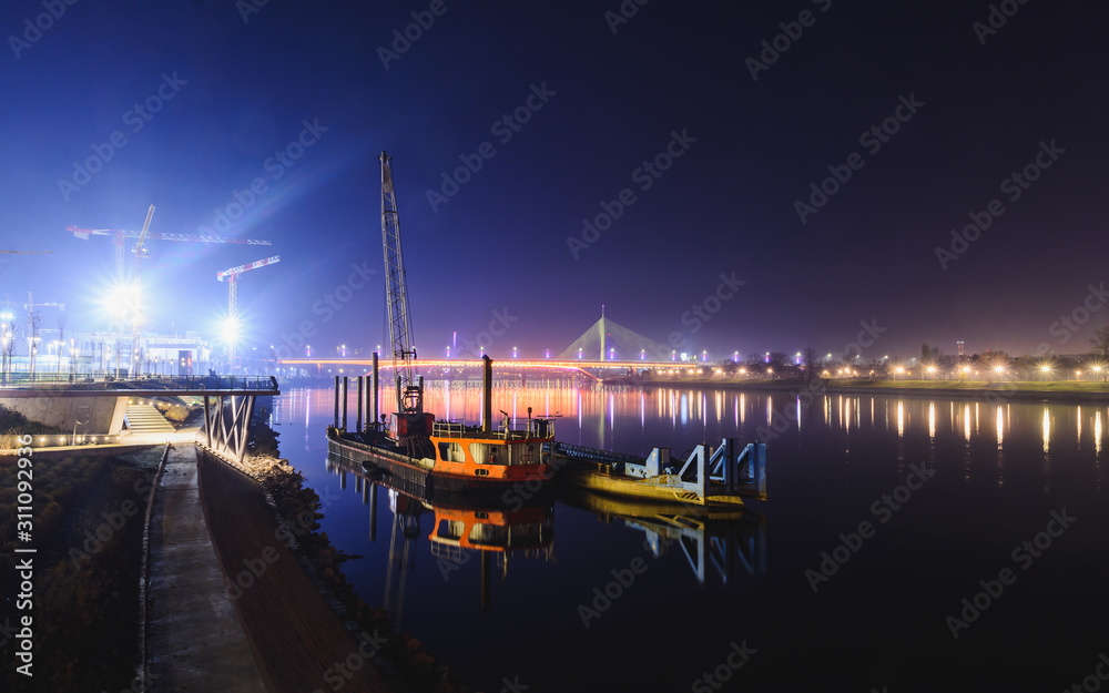 View on two ships reflected in the Sava river, distant Ada bridge and Gazelle bridge at night. Belgrade, Serbia.
