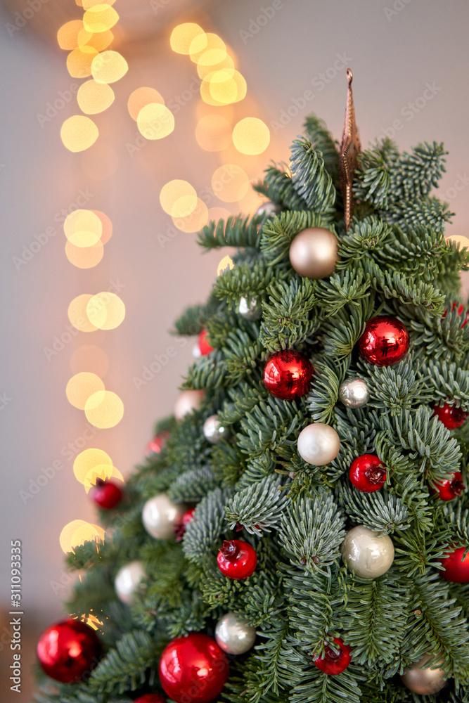 Beautiful small Christmas tree on wooden table. Happy mood. Garland lamp bokeh on background. Wallpaper. Danish pine and fir, Nobilis