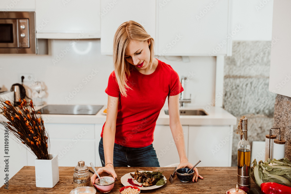 Beautiful blonde young woman cooking healthy food to stay fit and be in good healht. Relaxed and carefree. Lifestyle.