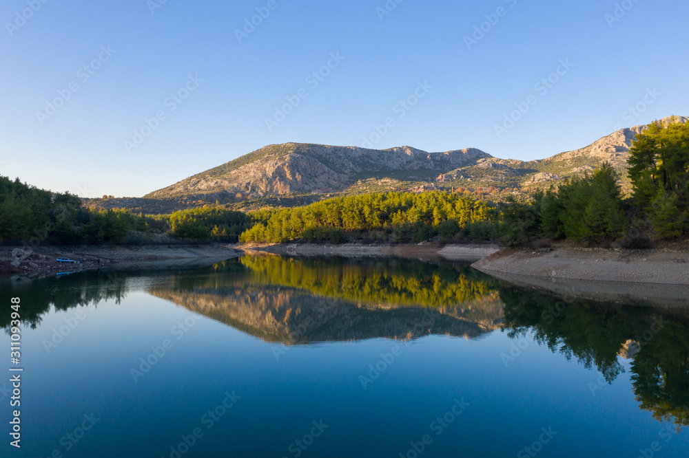 Natural lake surrounded by pine trees, mountains and a village.