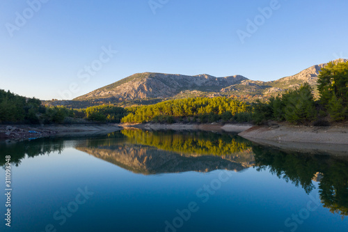 Natural lake surrounded by pine trees, mountains and a village.