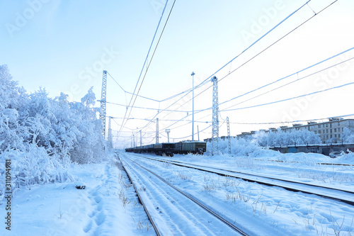 Snow-covered railway among the trees. Rails going into the distance. Freight cars standing on the rails. Winter landscape. Selective focus. 