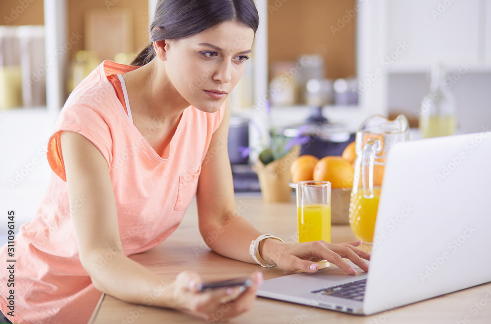 Pretty woman on the phone using laptop at home in the kitchen Pretty woman on the phone using laptop at home in the kitchen
