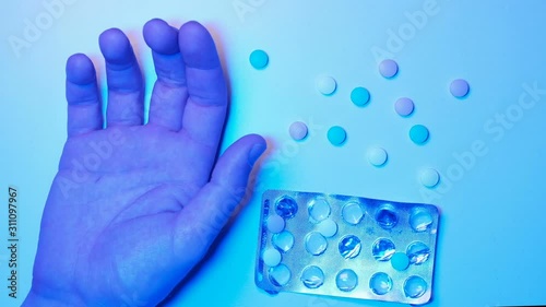 The right hand and pills on a white background lit by an ambulance siren. Flashing blue light. Close-up of a male palm and medicine. Concept of drug overdose or drug suicide.