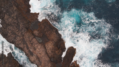 Aerial view - big waves break on the rocky coast of the Atlantic Ocean. A lot of sea foam. Volcanic rocks, Tenerife, Spain