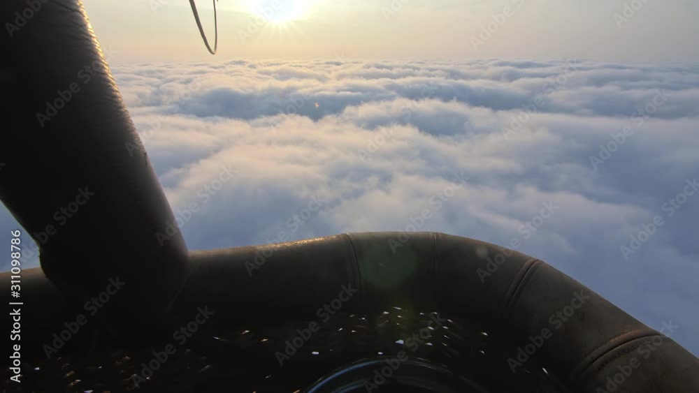 Adventure first person view, pov from basket of field, meadow, river and above cloud in flight on hot air balloon. The aircraft fly in morning blue sky. Hot air balloon burner flame into envelope.