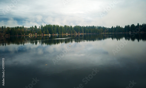 Lovely Lake Joy and the waterfront houses on a fog covered day with the surrounding trees and lingering clouds above reflecting in the water in the pacific northwest.