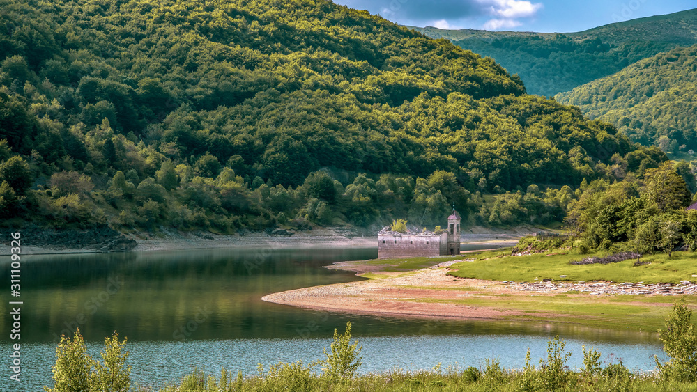 Landscape side view of old church of St Nicholas. Usually partially submerged in Lake. Spring in National Park Mavrovo, North Macedonia.
