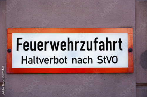 A red and white sign on a red, with the words "Feuerwehrzufahrt. Haltverbot nach StVO", translation: Driveway for fire brigade, Absolute stopping restriction, in black letters. © Boris