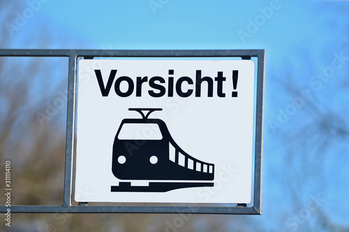 White sign with a black train icon and the German word for "Attention" (German: Achtung)