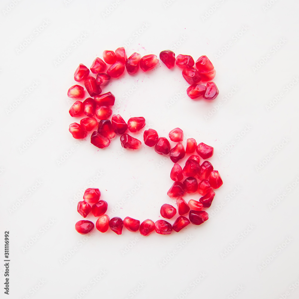 letter S folded from pomegranate berries on a white background top view