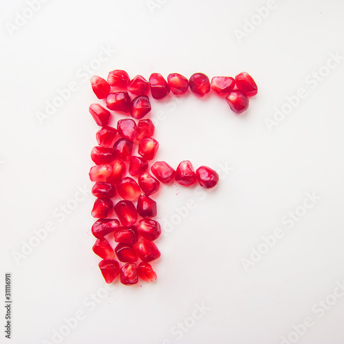 letter F folded from pomegranate berries on a white background top view
