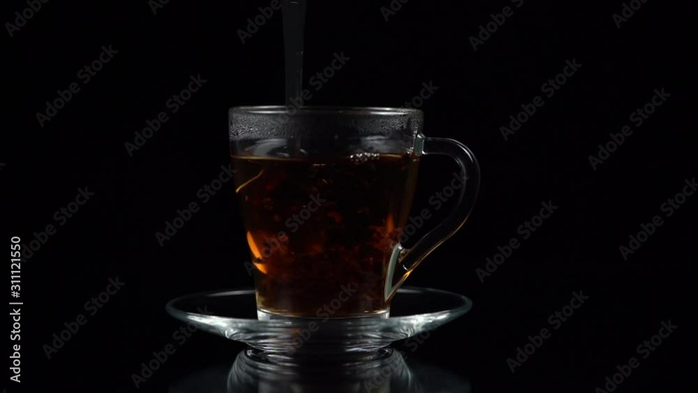 teaspoon stir hot tea with tea leaves in a tea Cup and saucer on a black background, slow motion teaspoon stir hot tea with tea leaves in a tea Cup and saucer on a black background, slow motion