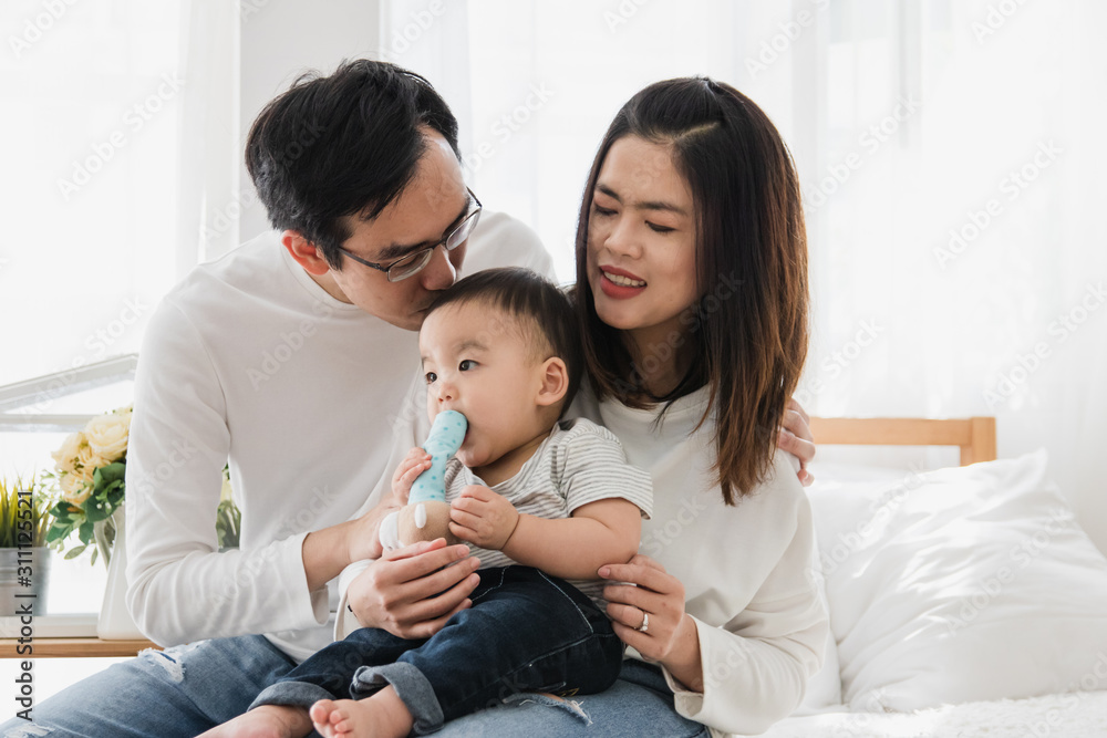 Happy asian family parents hug and kissing their baby boy in bedroom