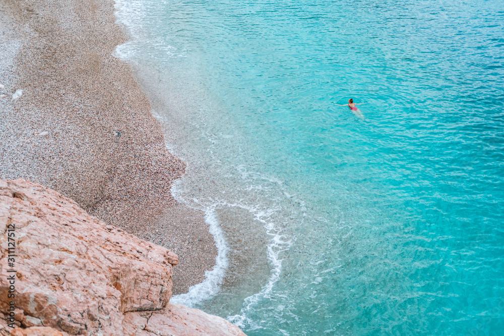 Obraz premium Girl in swimming in the azure clear sea on the pebble beach of the Adriatic sea. Shot from above.