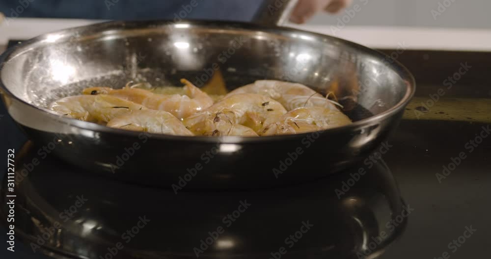 Close up of a chef preparing flambe dish shrimp on a frying pan. Oil and alcohol open flames. Restaurant kitchen concept. Chef tossings, mixing and throwing on pan prawns, close-up slow motion. Close up of a chef preparing flambe dish shrimp on a frying pan. Oil and alcohol open flames. Restaurant kitchen concept. Chef tossings, mixing and throwing on pan prawns, close-up slow motion.