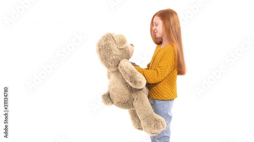 Close-up portrait of beautiful little girl with gorgeous red hair smiling and holding a big bear toy. Isolated, on white background. Happy childhood concept. True child emotions