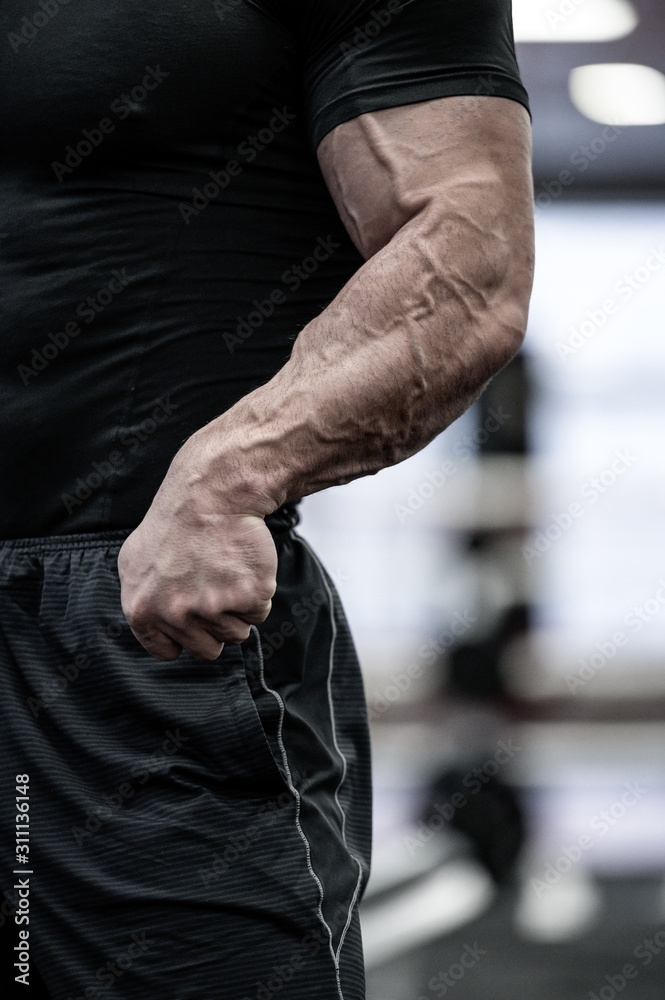 testosterone concept of body physique part of strong man in black sportswear showing strong arms with big vein during gym stress workout
