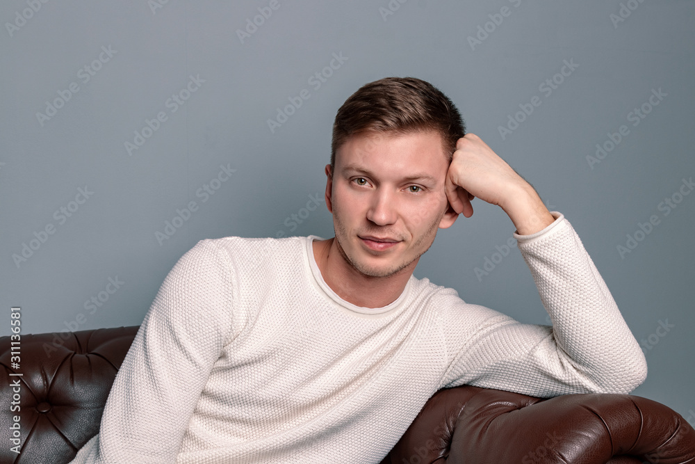 Handsome man wearing white sweater sitting on the leather sofa. Comfort and relaxation Handsome man wearing white sweater sitting on the leather sofa. Comfort and relaxation