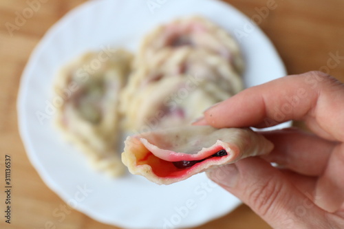 woman's hand holding bitten off dumplings with cherries above white plate with dumplings photo