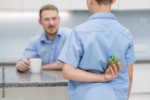 Young boy holds gift box behind his back for dad. Father day concept