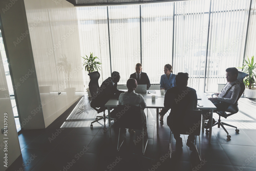 Obraz premium Silhouettes of people sitting at the table. A team of young businessmen working and communicating together in an office. Corporate businessteam and manager in a meeting
