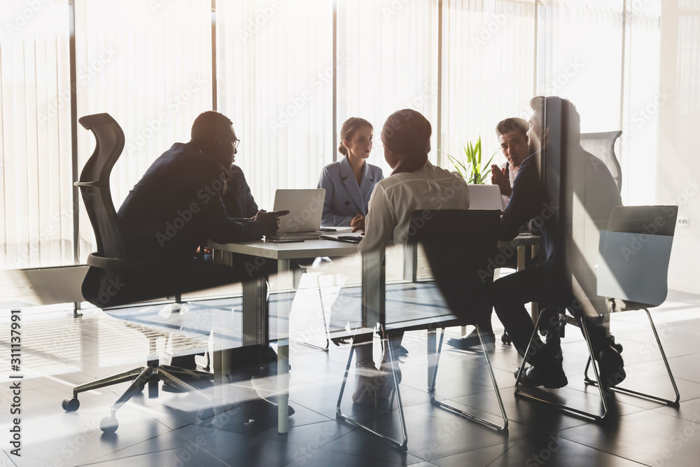 Silhouettes of people sitting at the table. A team of young businessmen working and communicating together in an office. Corporate businessteam and manager in a meeting Silhouettes of people sitting at the table. A team of young businessmen working and communicating together in an office. Corporate businessteam and manager in a meeting
