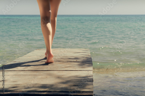 Fototapeta Naklejka Na Ścianę i Meble -  A girl walks on a bridge to the sea. The bridge on the beach. Beautiful legs and the sea.