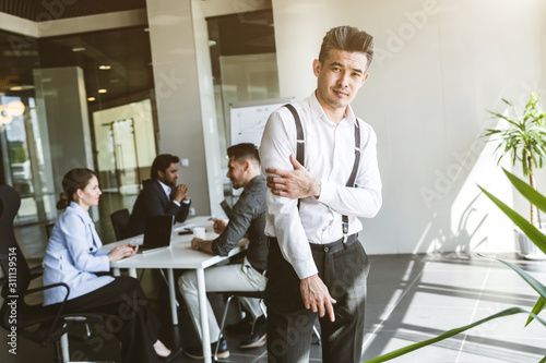 Business man stands on the background of partners. A team of young businessmen working and communicating together in an office. Corporate businessteam and manager in a meeting.