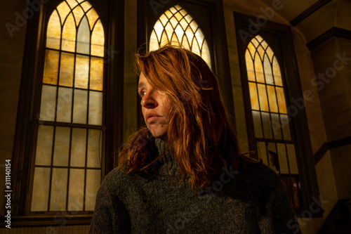 A young woman sits in a church with beautiful old stained glass