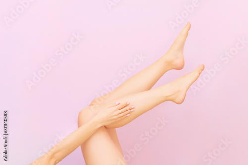 Beautiful long female legs with smooth skin after depilation on a pastel pink background. The concept of clean skin  waxing  shugaring  laser hair removal