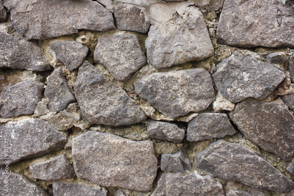 Fragment of an old stone wall made of gray rough stones. Textured background. Close up Fragment of an old stone wall made of gray rough stones. Textured background. Close up