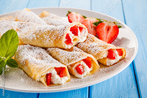 Sweet crepes with fruits on wooden table