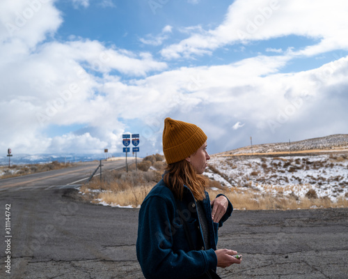 A woman in a mustard hat and blue vintage jacket on a road trip near the highway photo