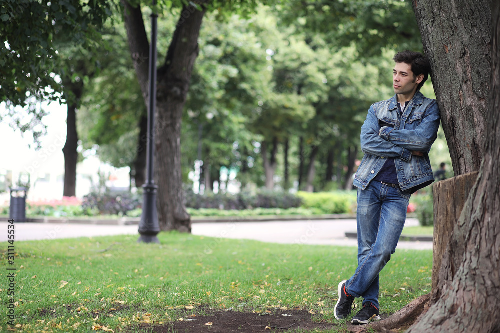 A young man walks in the park at lunch time. A man is on a walk in the city. A student in the park.
