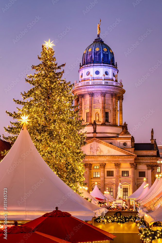 Fototapeta premium Blick auf den beleuchteten Deutschen Dom am Gendarmenmarkt in Berlin mit einem Weihnachtsbaum und Weihnachtsmarkt davor