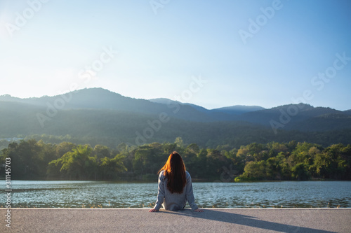 A woman sitting alone by the lake looking at the mountains with green nature background