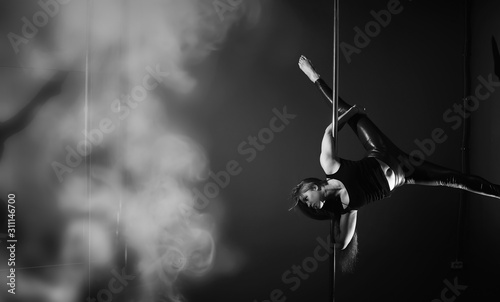 The dancer on the pylon in the studio. Girl doing exercises on a sports equipment.