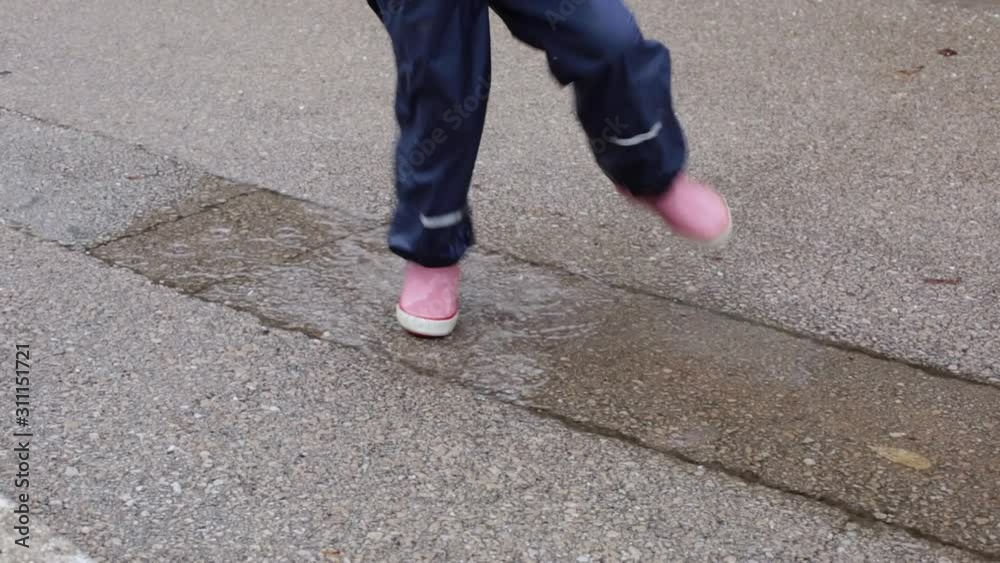 Girl child jumping in puddle splashing water in autumn rainy day Girl child jumping in puddle splashing water in autumn rainy day