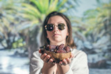 Woman in sunglasses holds out royal dates fruit in a bowl of coconut in a palm tree grove