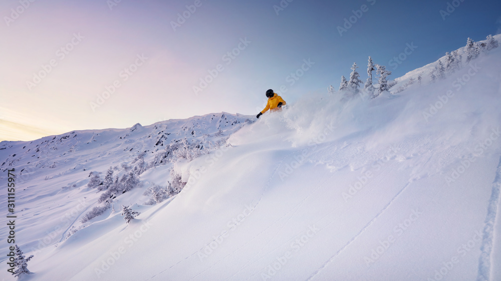at sunset, a freeride snowboarder unleashes a wave of snow